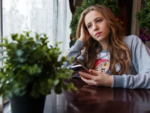 Ragazza pensierosa al telefono, con un'espressione che sembra dire "lei mi scrive e poi sparisce".