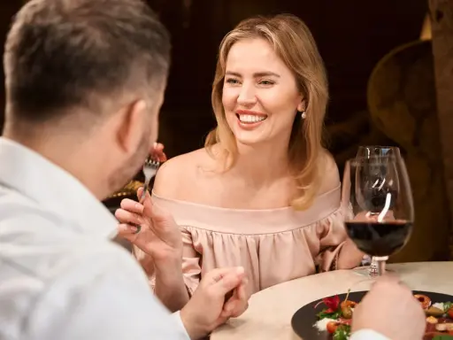 Coppia a cena, lei sorride mentre lui mangia. Forse stanno parlando di dove trovare sugar daddy per una vita di lusso.