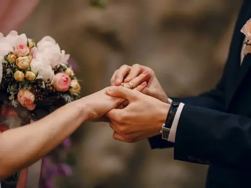 Scambio di fedi nuziali, un momento magico che ricorda un'agenzia matrimoniale gratis. Un bouquet di rose rosa e bianche completa la scena.