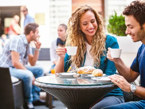 Coppia al bar, lei ride sorseggiando caffè. Un indizio di psicologia: come capire se un uomo è interessato?