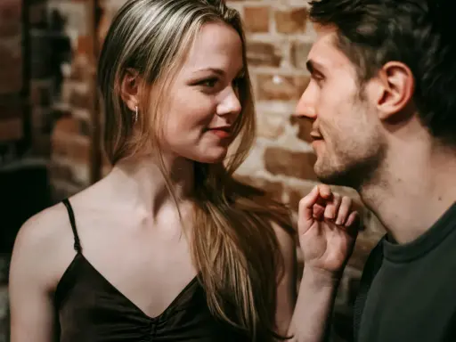 Un uomo e una donna si guardano intensamente. Lei ha lo sguardo di chi ti vuole, un sorriso accennato e i capelli biondi sciolti. Lui è vicino, con un'espressione concentrata.