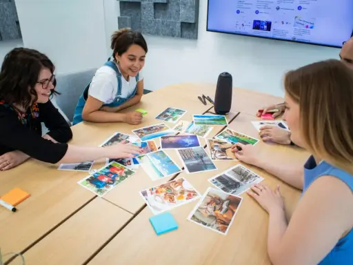 Persone attorno a un tavolo discutono immagini, trovando spunti di conversazione per un progetto creativo.
