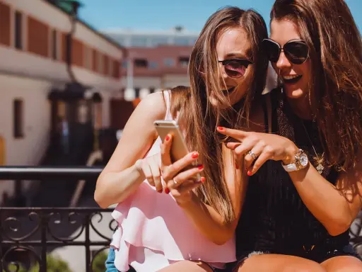 Due amiche ridono guardando il telefono, un momento perfetto per decidere cosa raccontare ad una ragazza.
