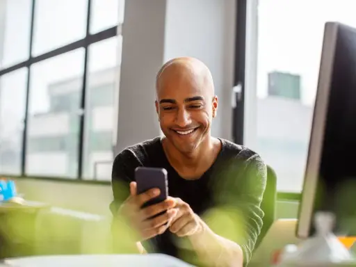 Uomo sorridente guarda il telefono, forse cercando frasi per approcciare qualcuno.