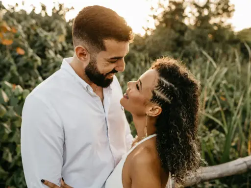 Un uomo e una donna si guardano con uno sguardo innamorato, circondati da una vegetazione lussureggiante al tramonto.