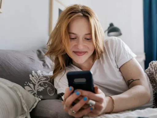 Ragazza con capelli rossi sorride guardando il telefono. Mi scrive ma non mi chiede di uscire, sperando in un invito.