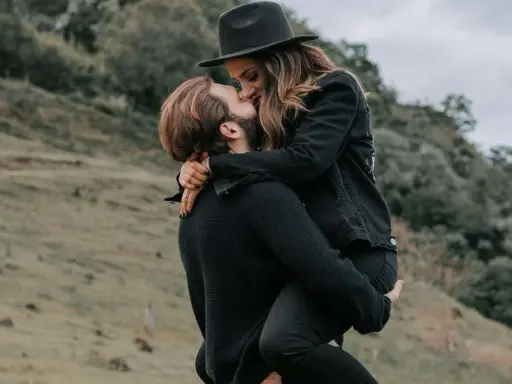 Coppia che si bacia appassionatamente all'aperto. Lui la solleva tra le braccia, lei indossa un cappello. Se ti chiede di uscire, gli piaci!