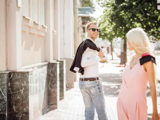 Un uomo sorride, voltandosi per guardarti negli occhi da lontano, con la giacca sulla spalla.