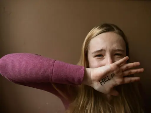 Ragazza con "HELP" scritto sulla mano, copre la bocca con espressione disperata. Un chiaro segnale di red flag relazione.
