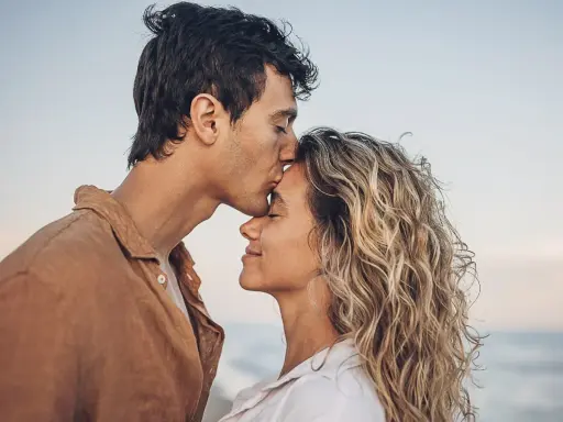 Un uomo bacia la fronte di una donna sulla spiaggia. Se una persona non ti cerca, forse è perché ha già trovato ciò che cercava.