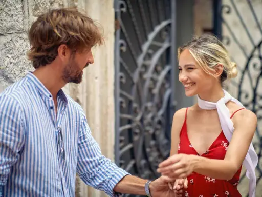 Un uomo con una camicia a righe fa l'occhiolino e sorride a una donna con un vestito rosso. Un momento di complicità.