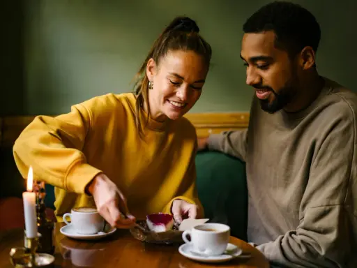 Coppia sorridente condivide un dolce, tra caffè e candela. Un momento intimo perfetto per porre domande da fare per conoscersi.