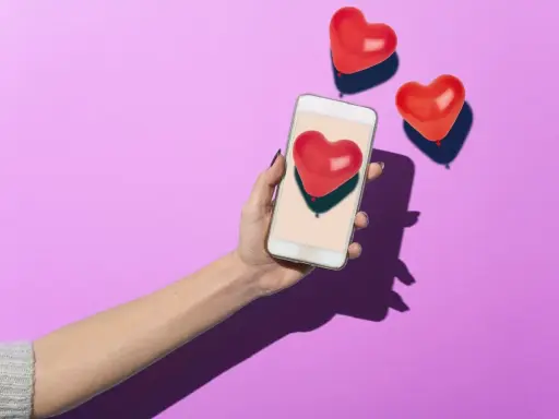 Mano con smartphone che mostra un cuore rosso, circondata da palloncini a forma di cuore. Simboleggia i comportamenti di un uomo non interessato, che ignora i segnali d'affetto.