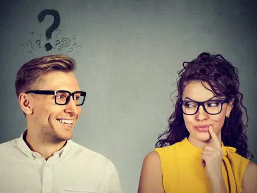 Uomo sorridente guarda donna pensierosa, con punti interrogativi sopra la testa. Come capire se gli piaci ma lo nasconde?