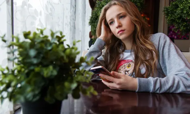 Ragazza pensierosa al telefono, con un'espressione che sembra dire "lei mi scrive e poi sparisce".