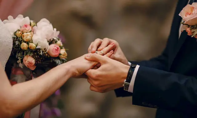 Scambio di fedi nuziali, un momento magico che ricorda un'agenzia matrimoniale gratis. Un bouquet di rose rosa e bianche completa la scena.