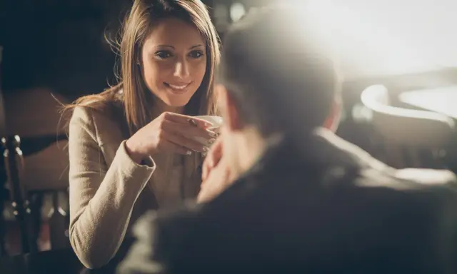 Lei sorride mentre beve un caffè, pensando a come chiedere di uscire per messaggio.