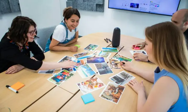 Persone attorno a un tavolo discutono immagini, trovando spunti di conversazione per un progetto creativo.
