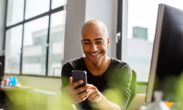 Uomo sorridente guarda il telefono, forse cercando frasi per approcciare qualcuno.