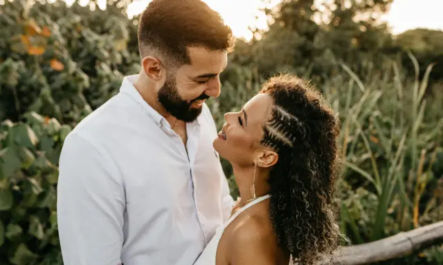 Un uomo e una donna si guardano con uno sguardo innamorato, circondati da una vegetazione lussureggiante al tramonto.