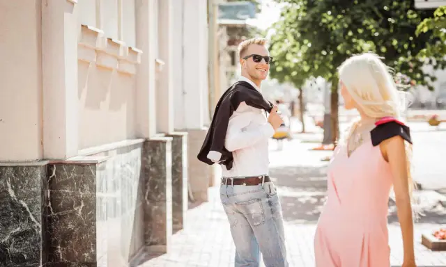 Un uomo sorride, voltandosi per guardarti negli occhi da lontano, con la giacca sulla spalla.