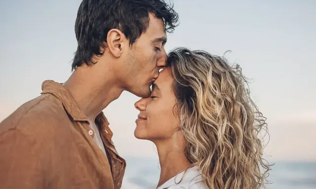 Un uomo bacia la fronte di una donna sulla spiaggia. Se una persona non ti cerca, forse è perché ha già trovato ciò che cercava.