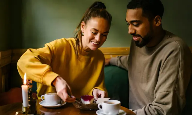 Coppia sorridente condivide un dolce, tra caffè e candela. Un momento intimo perfetto per porre domande da fare per conoscersi.