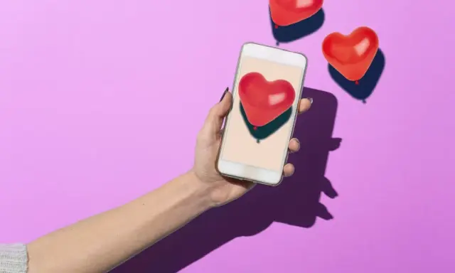 Mano con smartphone che mostra un cuore rosso, circondata da palloncini a forma di cuore. Simboleggia i comportamenti di un uomo non interessato, che ignora i segnali d'affetto.