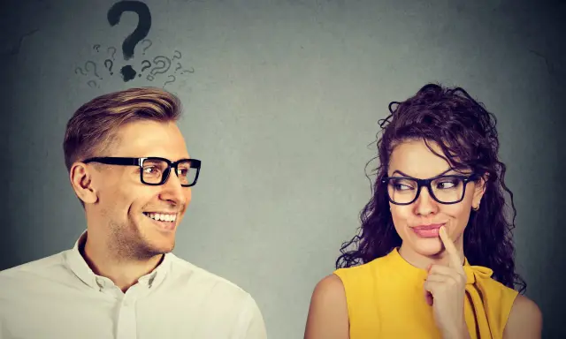 Uomo sorridente guarda donna pensierosa, con punti interrogativi sopra la testa. Come capire se gli piaci ma lo nasconde?