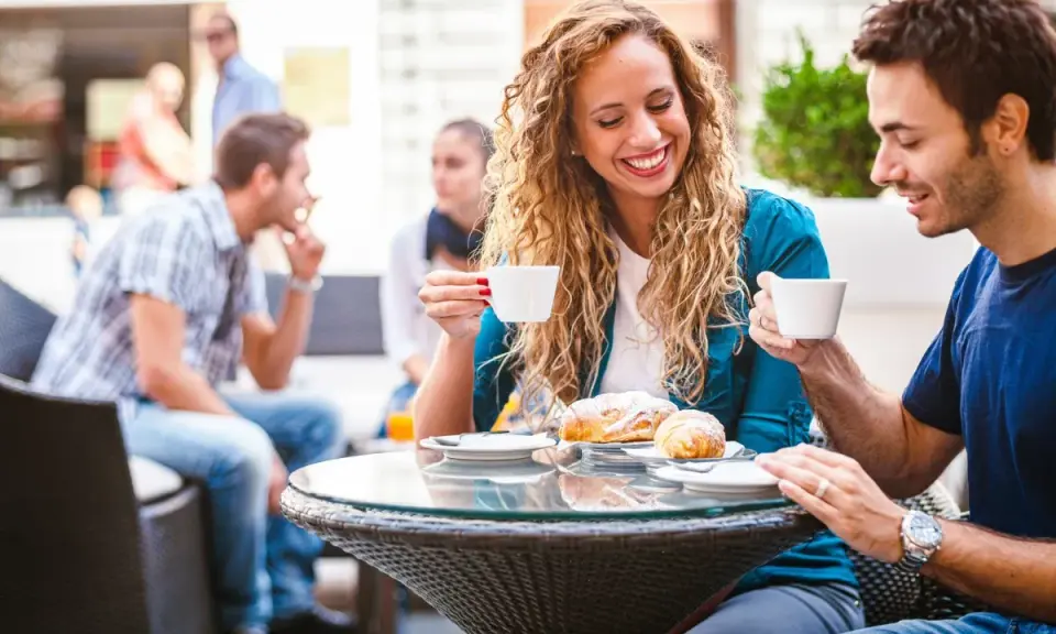 Coppia al bar, lei ride sorseggiando caffè. Un indizio di psicologia: come capire se un uomo è interessato?