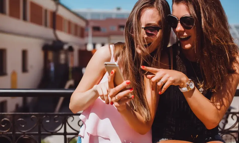 Due amiche ridono guardando il telefono, un momento perfetto per decidere cosa raccontare ad una ragazza.