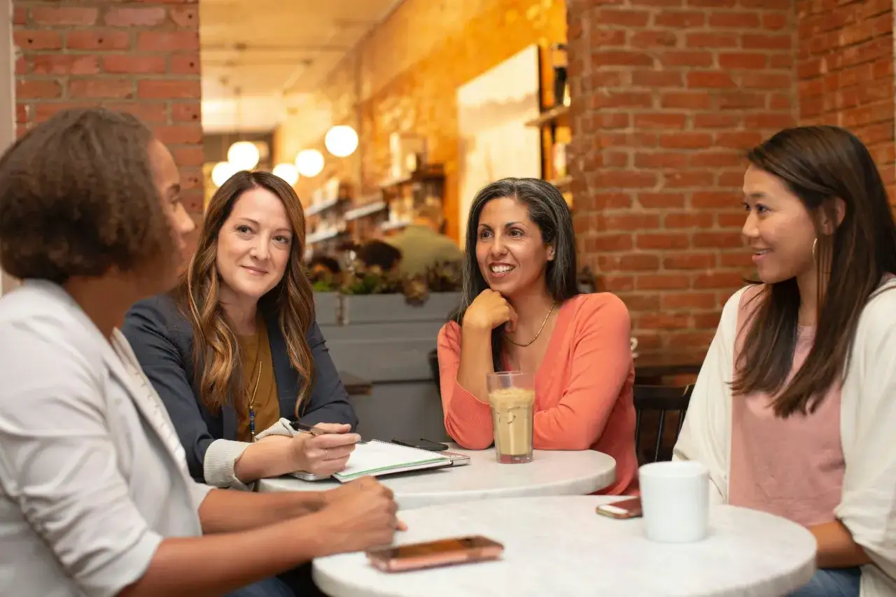 Quattro donne chiacchierano in un caffè. Una di loro scrive su un quaderno.