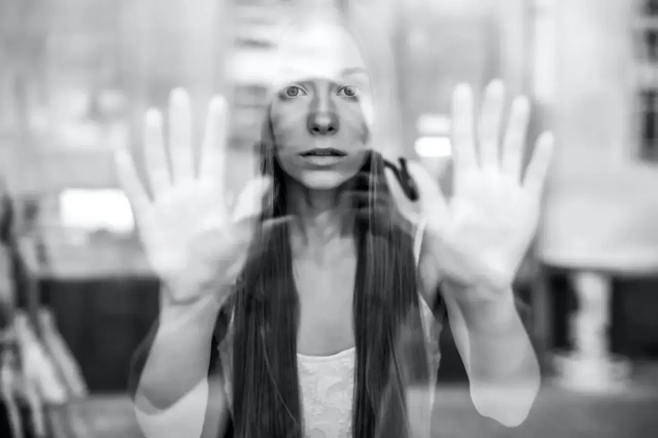 Ragazza spaventata dietro un vetro, mani tese. Un'immagine che evoca il disagio del catcalling, un reato che non va sottovalutato.