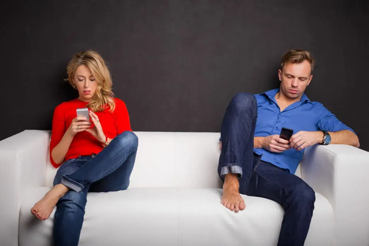 Coppia sul divano, ognuno assorto nel proprio smartphone, forse riflettendo su domande da farsi per conoscersi meglio.