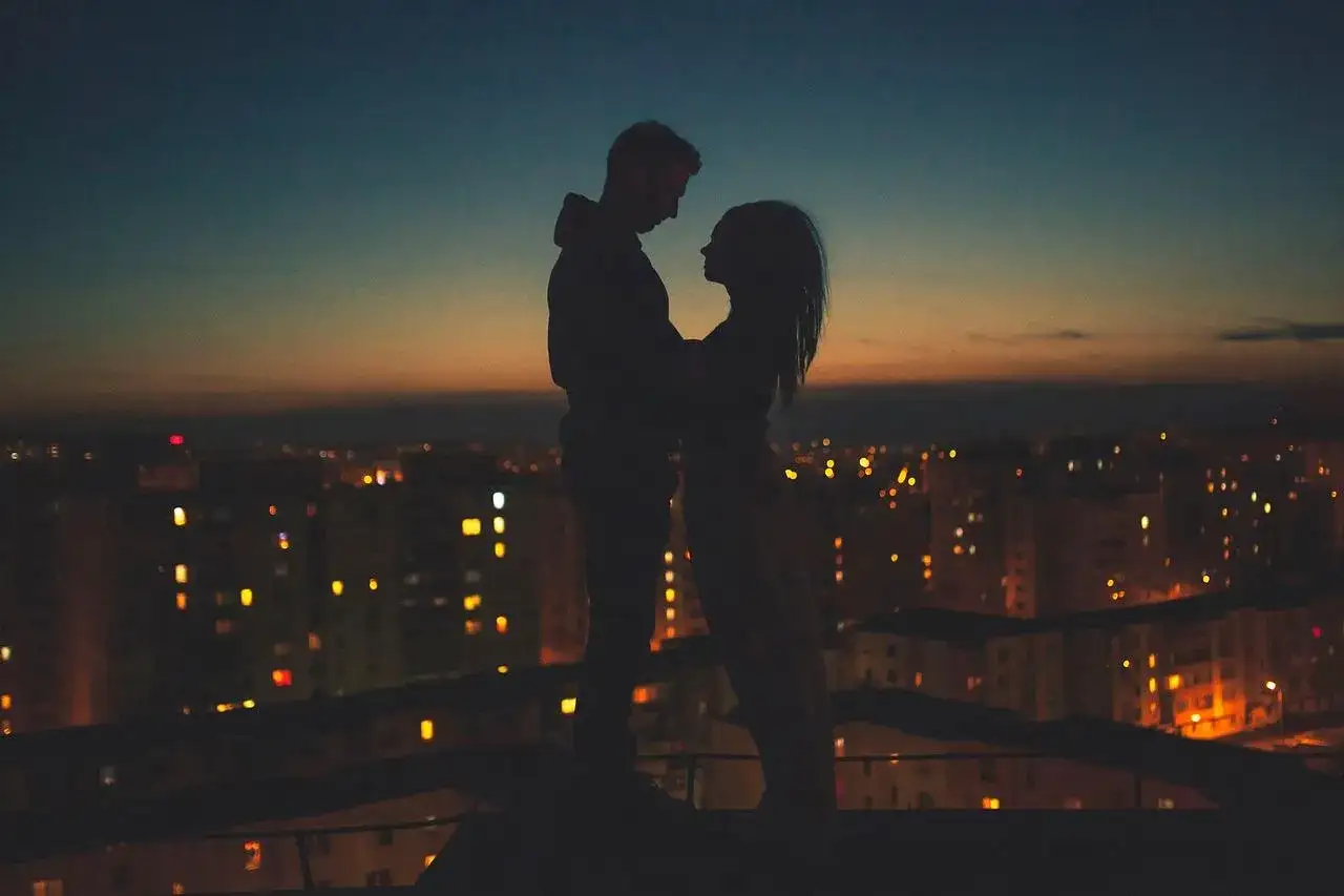 Coppia in silhouette sul tetto, la citt&agrave; illuminata sotto. Un momento magico quando lui ti guarda negli occhi in silenzio.
