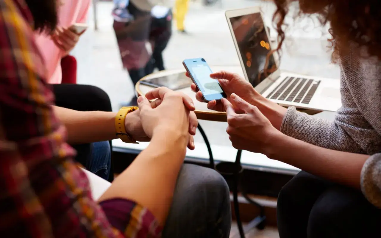 Due persone sedute vicine, una con un laptop, l'altra con uno smartphone, mentre fanno chat insieme.