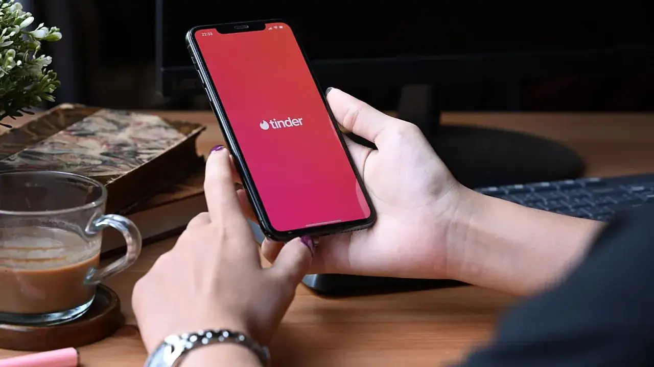 Mani che scorrono sull'app Tinder, un caffè e libri antichi sul tavolo. Chi usa Tinder cerca connessioni.