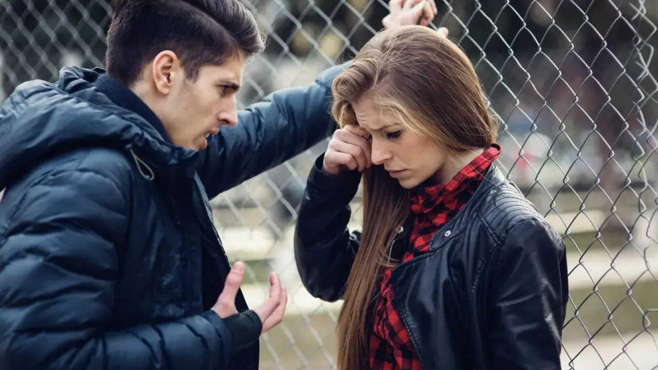 Un ragazzo parla con una ragazza triste appoggiata a una rete. Sembra un momento di tensione, forse un amore malato.