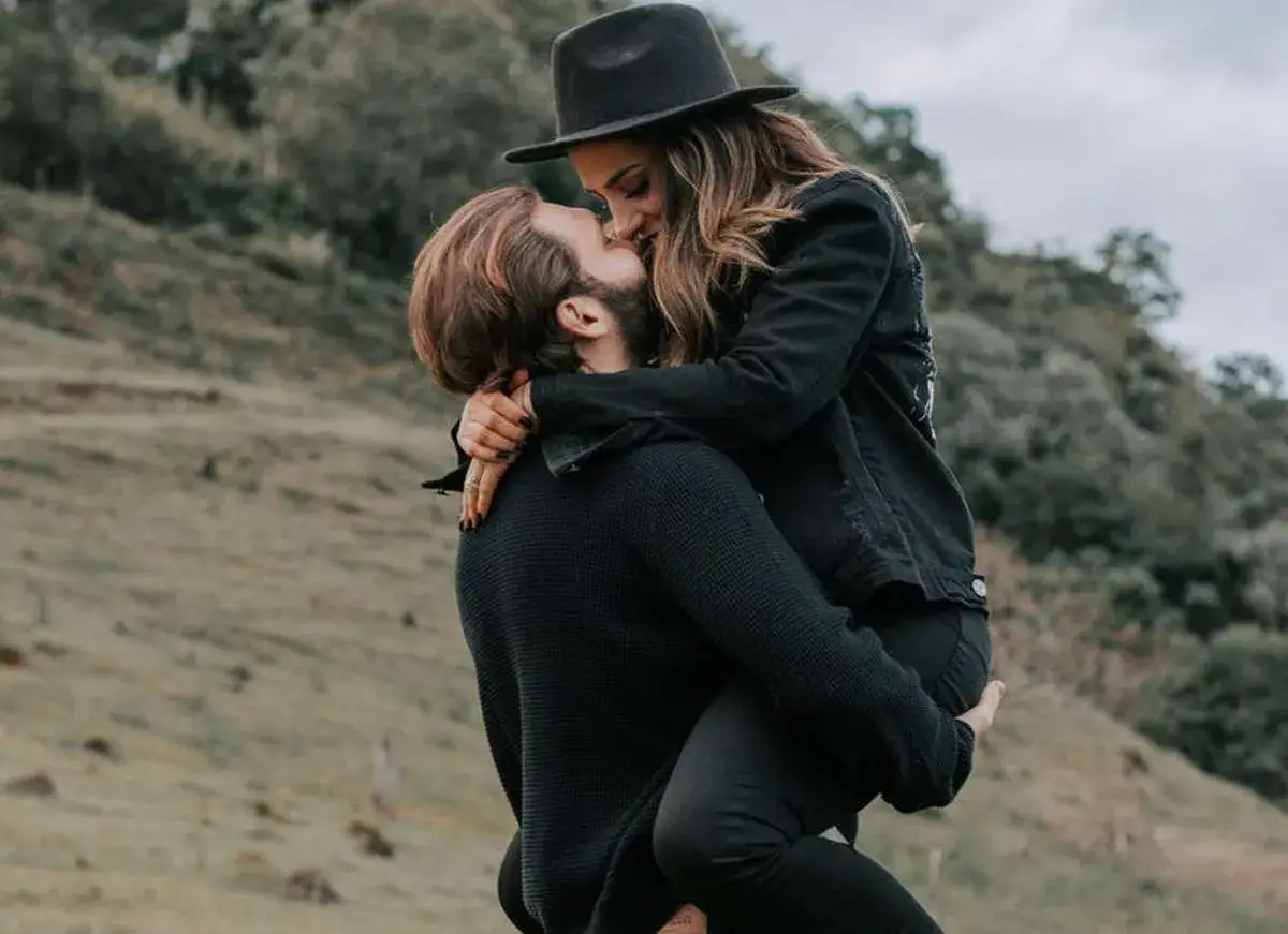 Coppia in un abbraccio appassionato, un uomo solleva una donna con un cappello. Segnali per capire se gli piaci ma lo nasconde.
