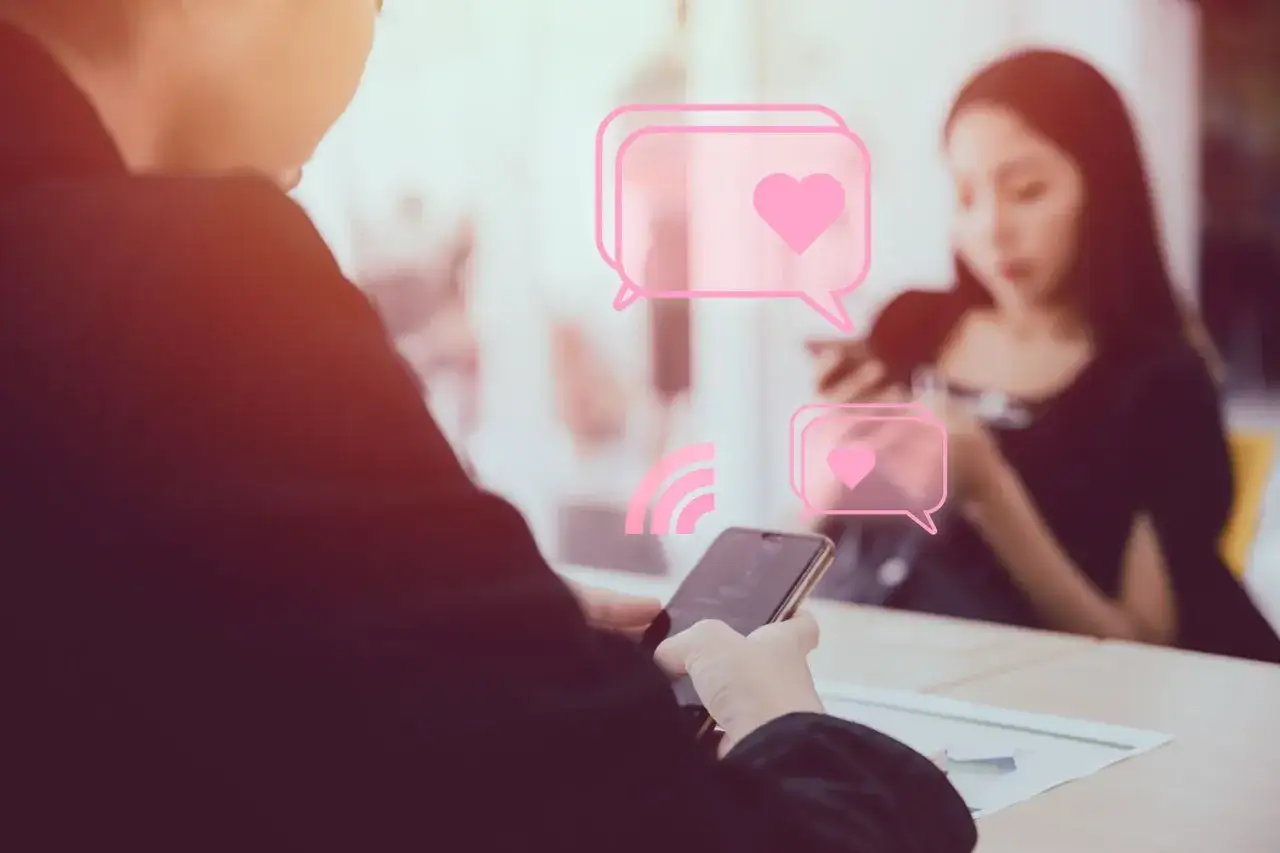 Una conversazione su Tinder in corso, con cuori rosa che fluttuano tra due persone che guardano i loro telefoni.