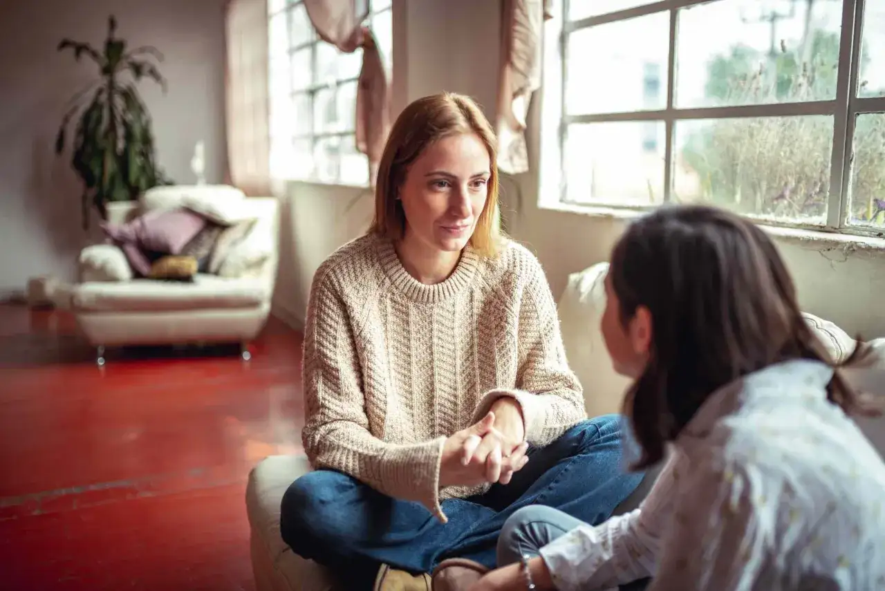 Due donne sedute in soggiorno, una ascolta attentamente l'altra. Un esempio di come fare conversazione in modo empatico.