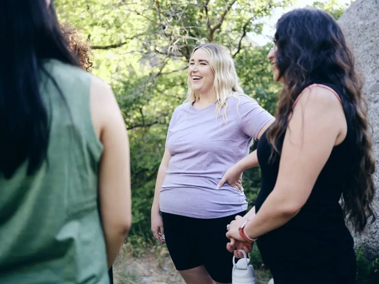Tre donne ridono all'aperto. Il linguaggio del corpo attrazione è evidente nel loro sorriso e nella vicinanza.