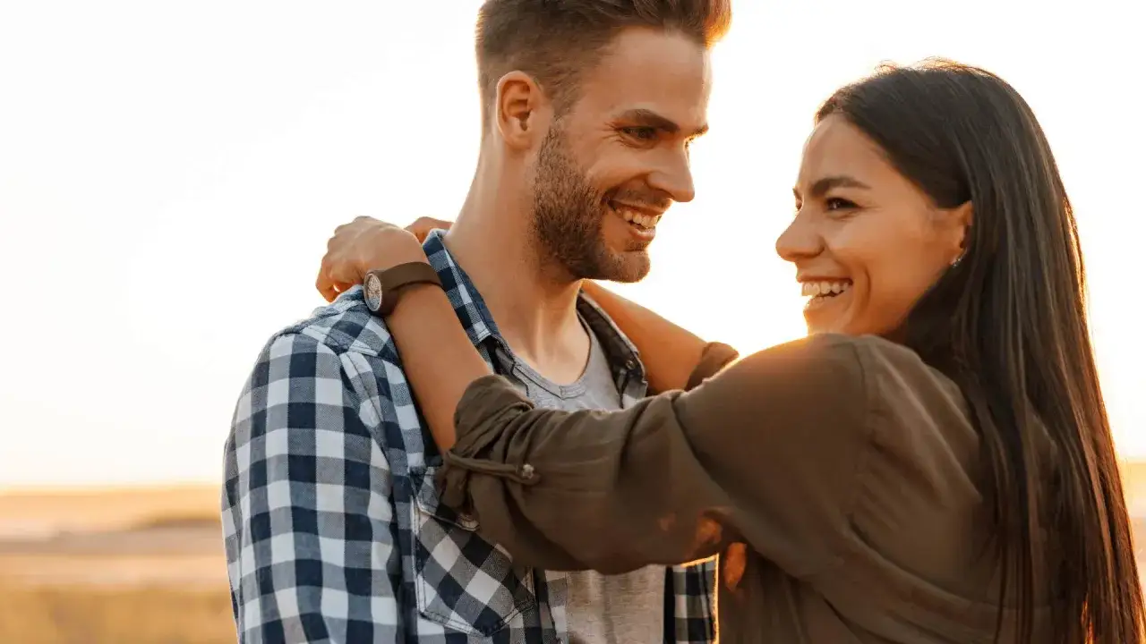 Coppia felice che si abbraccia al tramonto. Psicologia: come capire se un uomo è interessato? I sorrisi e il contatto visivo sono segnali chiave.