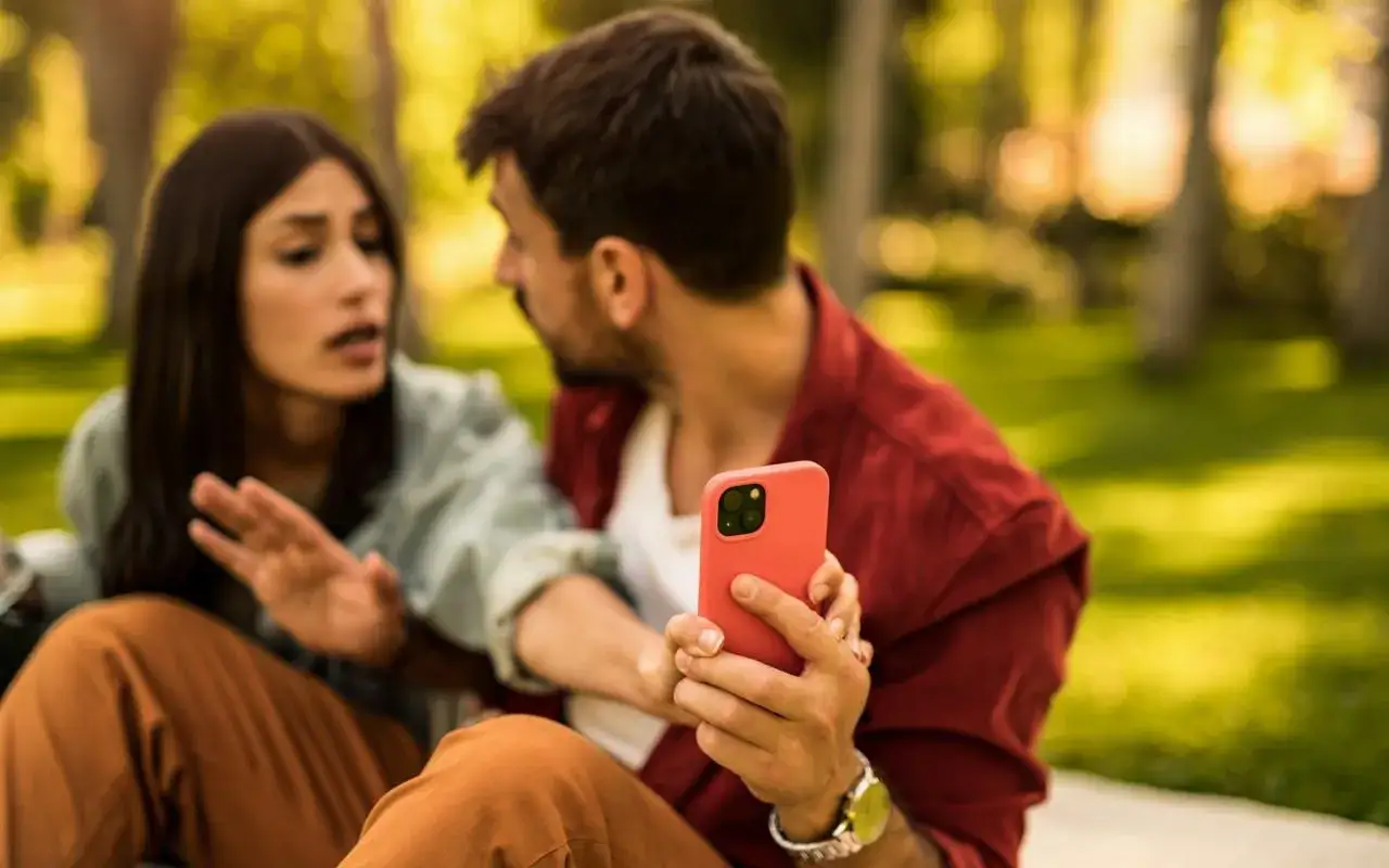 Una donna frustrata parla con un uomo che guarda il suo telefono, ignaro. La situazione è quella di quando un uomo non risponde ai messaggi.