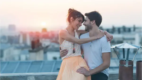 Coppia sul tetto al tramonto, sguardi complici e abbracci che rivelano segnali nascosti di attrazione.