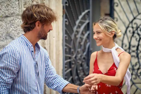 Un uomo con una camicia a righe fa l'occhiolino e sorride a una donna con un vestito rosso. Un momento di complicità.