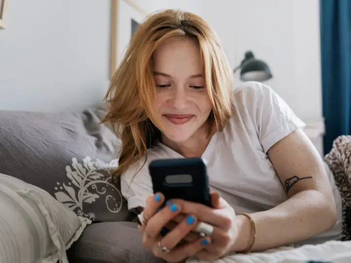 Ragazza con capelli rossi sorride guardando il telefono. Mi scrive ma non mi chiede di uscire, sperando in un invito.