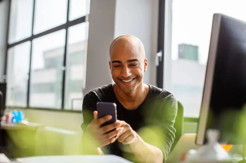 Uomo sorridente guarda il telefono, forse cercando frasi per approcciare qualcuno.